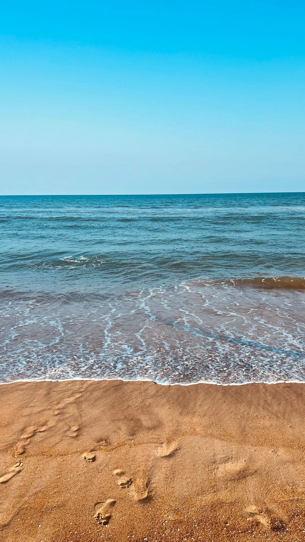 Footprints on a beach with blue water and clear sky